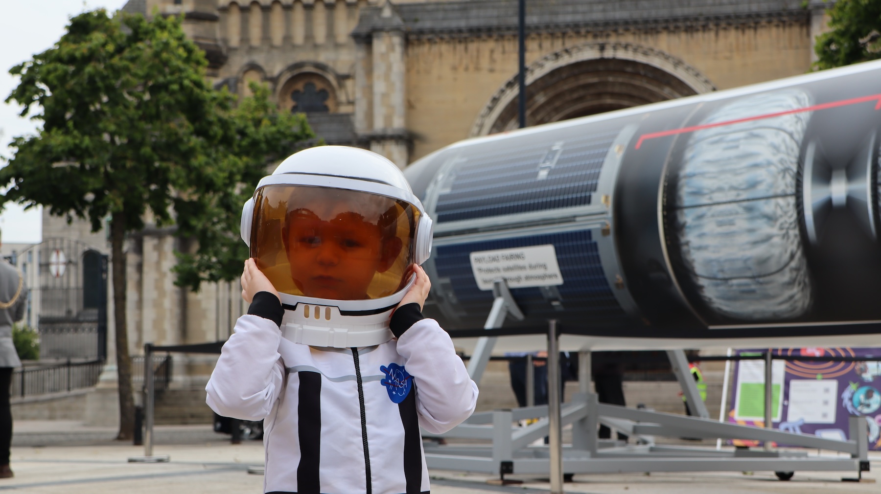 A young visitor to space for everyone is shown tryng on a space suit, in front of a rocket.